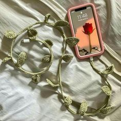 a cell phone laying on top of a white bed next to a cord with a flower