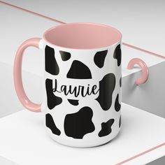 a black and white cow print coffee mug with pink handles sitting on top of a shelf