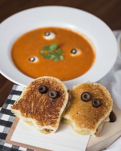 two toasted sandwiches with googly eyes sit on a plate next to a bowl of soup