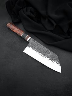 a large knife sitting on top of a black cloth covered table next to a piece of cloth