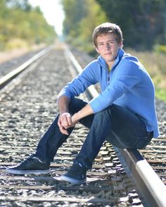 a young man sitting on train tracks with his hands in his pockets and looking at the camera