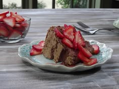 a piece of chocolate cake with strawberries on the plate next to it and a bowl of strawberries