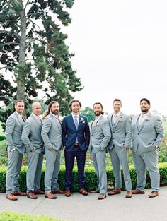 a group of men in suits standing next to each other on a cement ground near bushes and trees