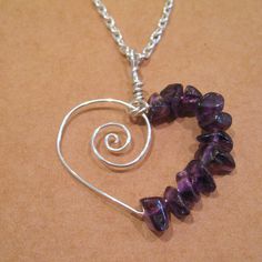 a heart shaped necklace with amethyst beads and silver wire on a brown background