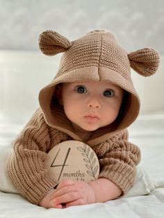 a baby is wearing a bear sweater and holding a sign with the number 4 on it