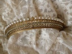 three gold and pearl bracelets are laying on a lace covered surface, with white lace in the background