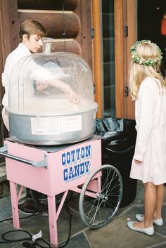 two children standing in front of a cotton candy machine with a girl looking at it