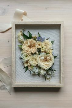 a white frame with flowers in it and a ribbon on the floor next to it