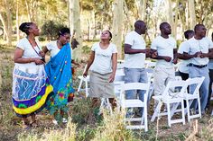 a group of people standing next to each other near white chairs in the grass and trees