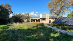 a house with solar panels on the roof and grass in front of it, surrounded by trees