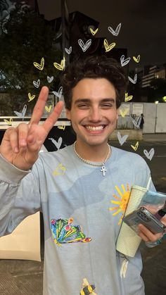 a young man is making the peace sign with his hand and holding a cell phone