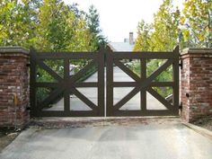 an iron gate with brick pillars and gates on either side, leading to a driveway