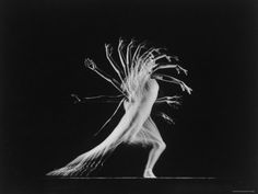 a black and white photo of a woman with long hair in motion on a dark background