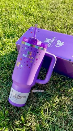 a purple starbucks cup sitting in the grass next to an open box on top of it