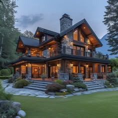 a large house that is in the middle of some grass and trees with lights on it