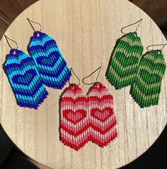 three beaded heart shaped earrings hanging on a wooden board with string attached to them