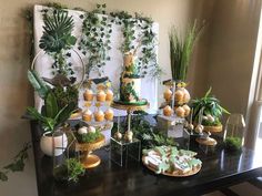 a table topped with lots of cakes and desserts covered in greenery next to a window