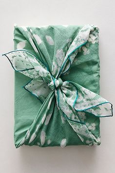 a wrapped present sitting on top of a white table next to a green napkin with a bow