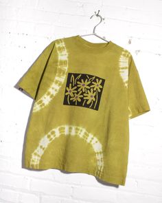 a t - shirt hanging on a white brick wall with a black and yellow tie dye design