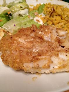 a white plate topped with chicken and rice next to a green leafy salad on top of a wooden table