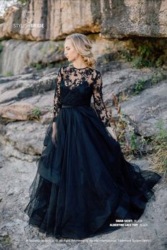 a woman in a black dress standing on rocks