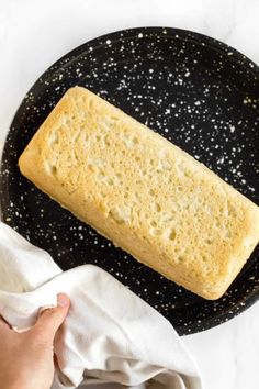 a piece of bread on a black plate next to a white napkin and a person's hand