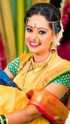 a woman in yellow and green sari with gold jewelry on her head, smiling at the camera