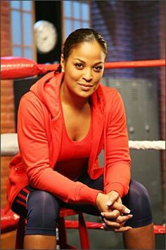 a woman sitting on top of a chair next to a boxing ring with a clock in the background