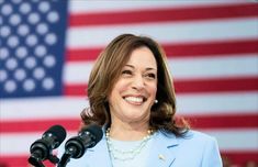 a woman standing at a podium in front of an american flag and holding a microphone