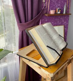 an open book sitting on top of a wooden table next to a purple wallpaper