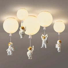 an astronaut themed ceiling light fixture with five lights attached to it, and three astronauts hanging from the ceiling