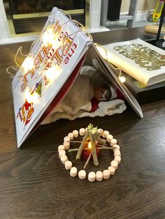 an open book on top of a wooden table next to a candle and some beads