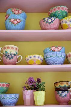 colorful cups and bowls on shelves with flowers in them