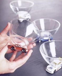 a hand is holding a toy car in front of three glass bowls on a table