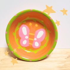 an orange and green plate with a pink butterfly design on it sitting on a wooden table