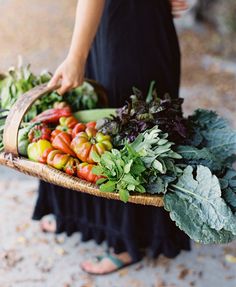 a woman holding a basket filled with lots of fruits and vegetables on top of it