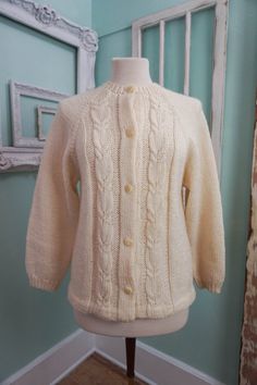 A classic women's cardigan sweater, in a soft ivory white acrylic. It has a unique wide pattern of traditional cable knit down the front. It closes up the front with a row of really unique swirly plastic buttons. The sweater is soft and comfy, not stiff at all. No damage or issues. Please check measurements carefully. Condition: Very Nice Vintage Tag: 100% Acrylic Size L Measurements in inches.... Length: 23.5 Chest: 19 ✩ Because you don't want to miss a thing, follow @heartkeyologie on Facebook Elegant Cream Cable Knit Cardigan, Classic Fitted Knitted Cardigan, Classic Knit Cardigan For Winter, Fitted Cream Sweater With Buttons, Classic Hand Knitted Sweater For Winter, Fitted Cream Knitted Outerwear, Fitted Classic Sweater In Winter White, Classic Beige Cable Knit Cardigan, Fitted Classic Winter White Sweater