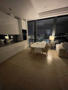 a living room filled with furniture and a large window overlooking the city at night time