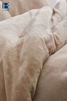 an unmade bed with beige sheets and pillows