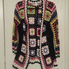 a colorful crocheted jacket hanging on a white door hanger in front of the door