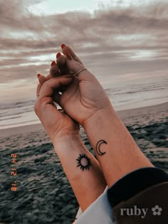 two people holding hands with tattoos on their wrists and the ocean in the back ground