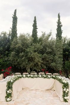 an outdoor table set up with flowers and greenery