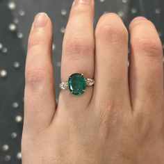 This rare and beautiful green emerald and diamond ring is perfect for any modern engagement! This oval cut emerald marquise diamond ring is finished in 14 karat yellow gold. Sleek modern in design. The center emerald reflects a rich sea green hue. Two (2) sparkling accent diamonds flank the center gemstone. Full of sparkle vibrant color. Finished on a classic 14 karat yellow gold band with a geometric gallery rail. Colored gemstone engagement rings add a personal touch to your special ceremony. Green Oval Ring, Wedding Ring With Emerald Accents, Oval Cut Emerald Engagement Ring, Emerald Oval Ring, Emerald Oval Engagement Ring, Oval Emerald Ring Design, Emerald Stone Engagement Ring, Emerald Green Engagement Ring, Emerald Engagement Ring Oval