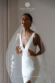 a woman in a white wedding dress and veil smiles as she stands with her hands on her hips