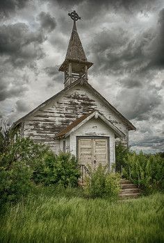 an old wooden church with a steeple and cross on the roof is surrounded by tall grass