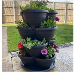 a stack of black planters filled with flowers on top of a stone patio area