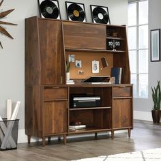 a wooden desk with an open bookcase and record player on top, in front of a large window