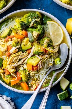 two bowls filled with noodles, broccoli and carrots next to lemon wedges