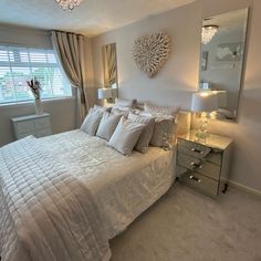 a white bed sitting in a bedroom next to a window covered in curtains and pillows