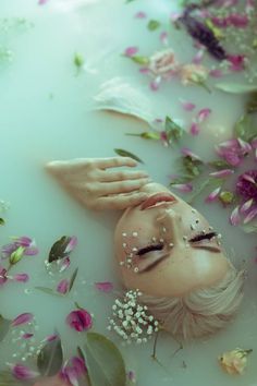 a woman laying in a bath filled with water surrounded by pink and white flower petals